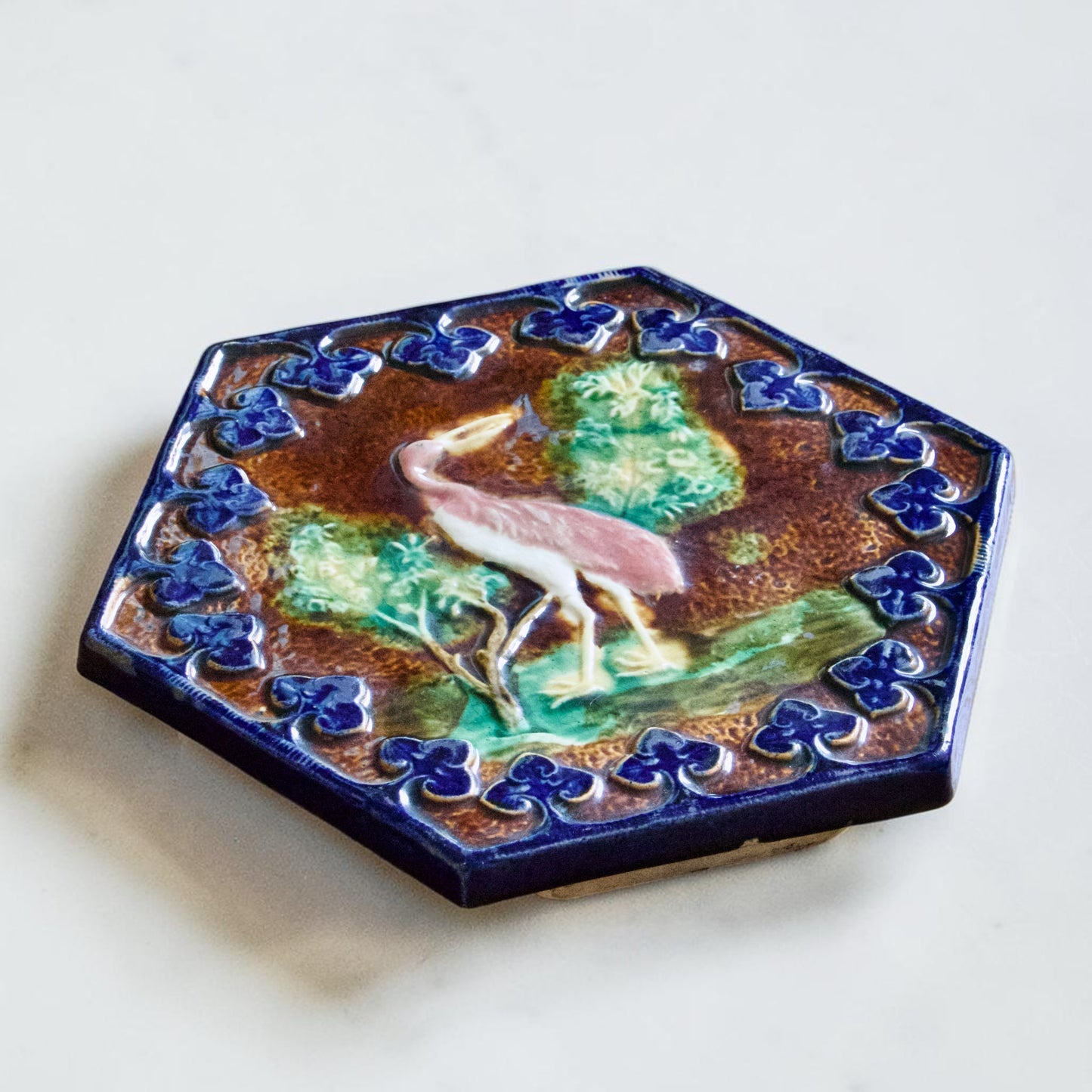 Dessous de plat XIXe en barbotine polychrome oiseau rose